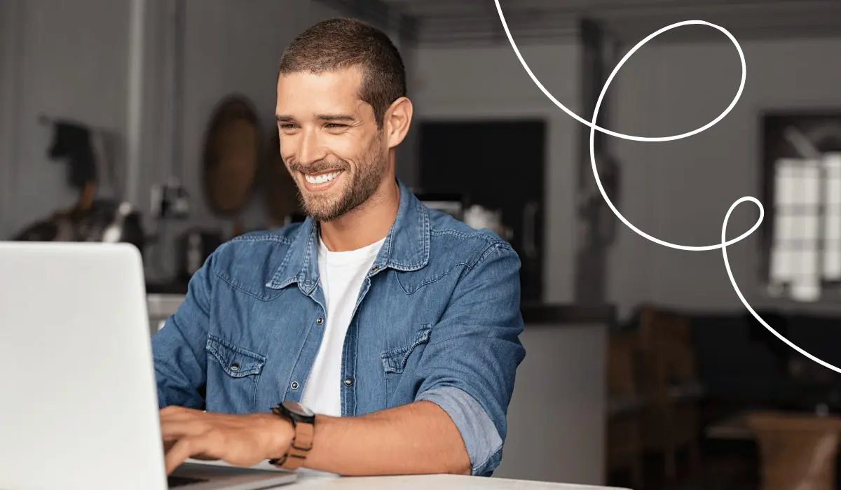 A young man is working on a laptop in a café and smiling