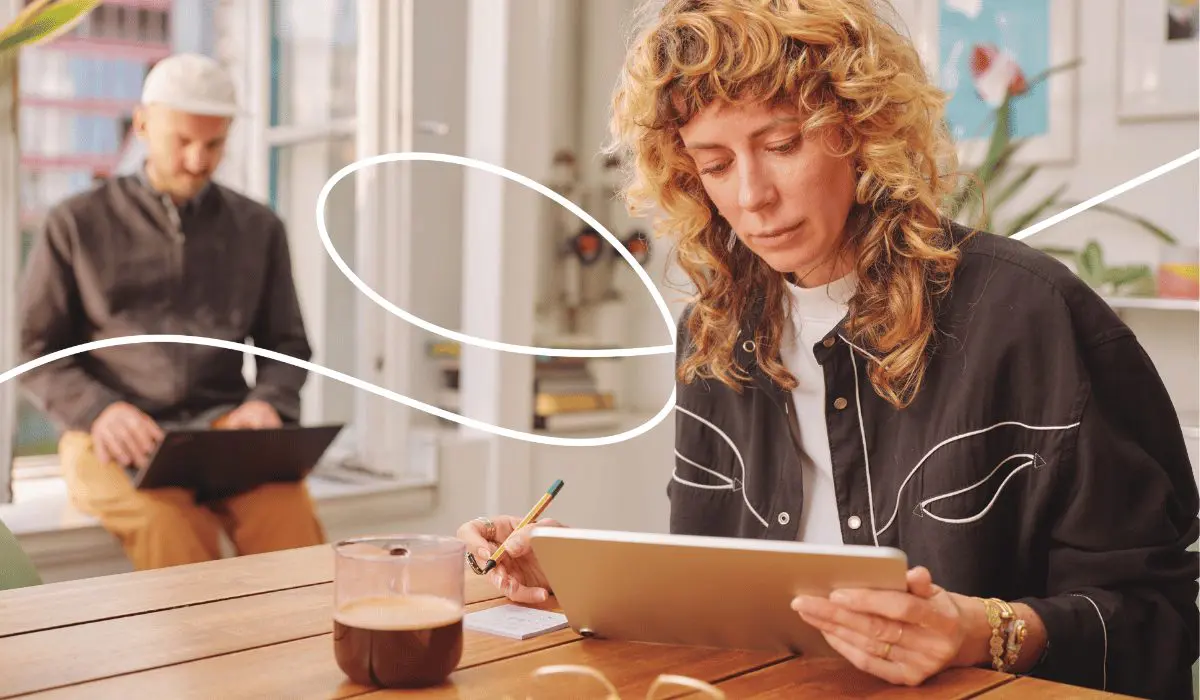 A woman is sitting at a table, working on a tablet