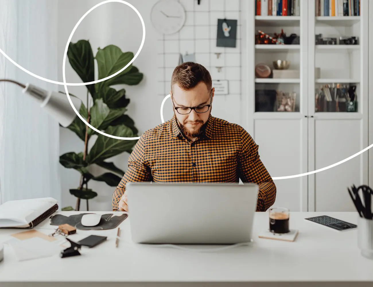 A man in a plaid shirt is sitting at a laptop in an office, staring intently at the screen.