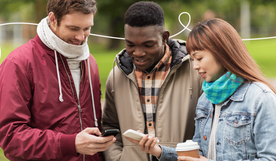 Drie jongeren kijken in het park naar hun smartphones – een typisch gebruiksscenario voor digitale loyaliteitsprogramma's.