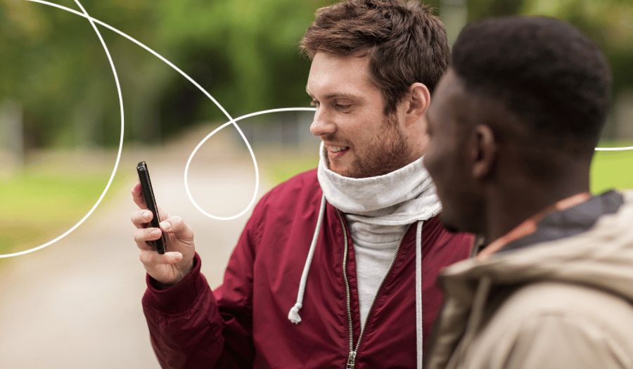 Zwei junge Männer stehen in einem Park und reden miteinander während sie auf ein Smartphone schauen. Symbolbild für Kundenfeedback per App.