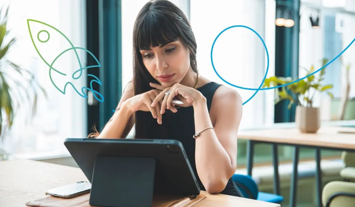 Junge Frau sitzt in einem hellen Büro und schaut konzentriert auf ein Tablet. Sie überlegt, welche Loyalty Features für ihr Treueprogramm wichtig sind.
