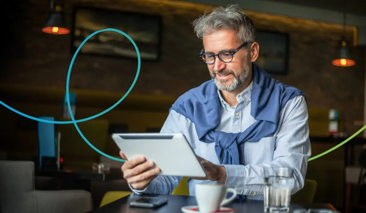 Älterer Mann mit Brille und grauen Haaren arbeitet an einem Tablet. Er sitzt an einem Tisch, neben ihm eine Kafeetasse. Er schaut freundlich aber konzentriert. Symbolbild für eine Person, die sich mit Datenschutz in Loyalty Apps auseinandersetzt.