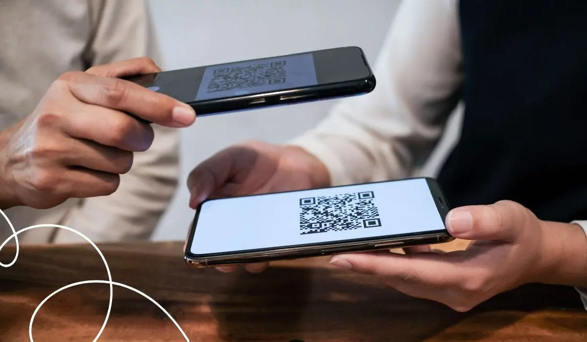 Dwie osoby trzymają w rękach smartfony. Jedna z nich skanuje kod QR za pomocą swojego telefonu z ekranu telefonu drugiej osoby.