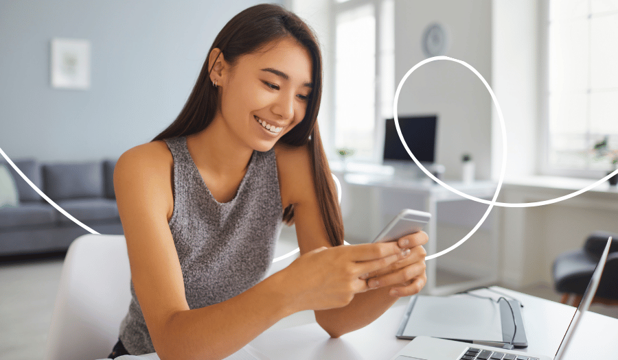 Una joven está sentada en una mesa y escribe en un smartphone. Sonríe.