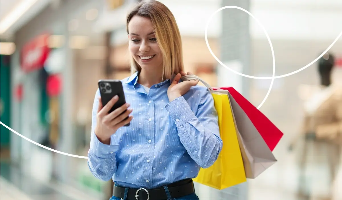 Junge Frau steht in einem Kaufhaus mit Einkaufstaschen in der Hand und schaut auf die Loyalty App in ihrem Smartphone.