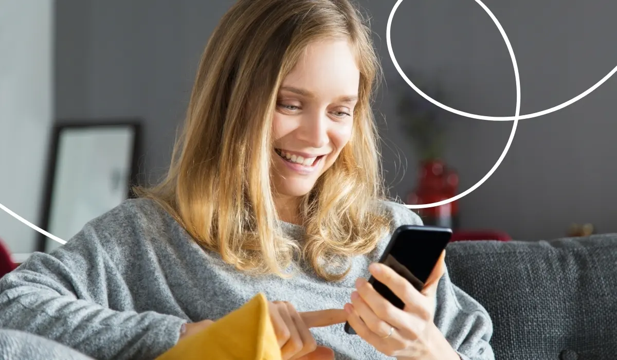 A young woman looks at her cell phone with a smile and types out a review for an app.