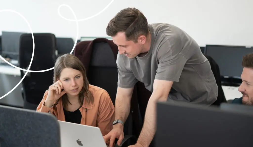 Two members of the IT team are looking at a laptop and talking to each other.