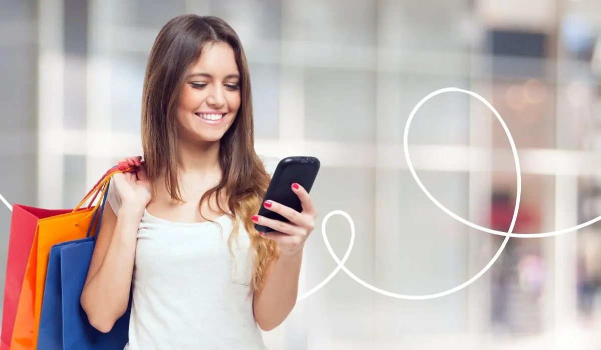 A young woman looks at a loyalty program on her smartphone while standing in a shopping mall with shopping bags, in the middle of shopping.
