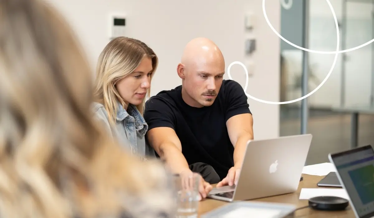 Twee medewerkers van hello again uit het onboardingteam zitten in een kantoor aan een bureau voor een laptop en bespreken iets.