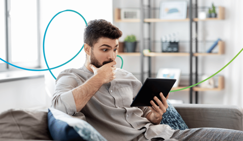Mann sitzt auf einem Sofa und schaut erstaunt auf ein Tablet